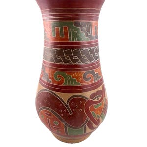May include: A tall, handcrafted ceramic vase with a wide rim and a bulbous body. The vase features intricate, colorful designs in shades of red, orange, green, and beige. The patterns include geometric shapes and stylized figures, showcasing a traditional aesthetic.