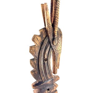 Puede incluir: Una escultura de madera de una cabeza de animal estilizada con un pico largo tallado. La escultura es de color marrón oscuro y tiene una superficie texturizada.