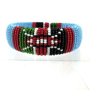 May include: A beaded bracelet with a colorful design that resembles the Kenyan flag. The bracelet is made of small, round beads in shades of blue, red, green, black, and white.