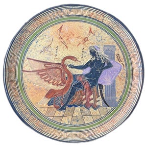 May include: A round ceramic plate with a green and black border. The center of the plate features a painted image of a woman sitting on a throne with a swan beside her. The woman is wearing a purple robe and has long black hair. The swan is red and white with black wings. The background is a light orange color with a geometric pattern.