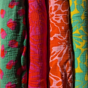 Puede incluir: Primer plano de cuatro rollos de tela colorida. Las telas presentan varios patrones, incluyendo diseños florales y abstractos, en tonos de verde, rosa, naranja y amarillo. La tela tiene una apariencia texturizada y arrugada.