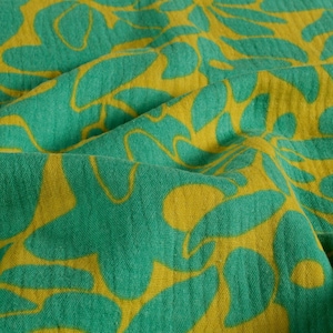 May include: Close-up of a fabric with a repeating floral pattern. The design features large, stylized leaves in a vibrant yellow against a teal green background. The fabric has a soft, textured appearance, with visible folds and shadows.