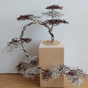 May include: A wire sculpture of a bonsai tree with brown and silver wire branches and leaves. The tree is mounted on a small wooden base.