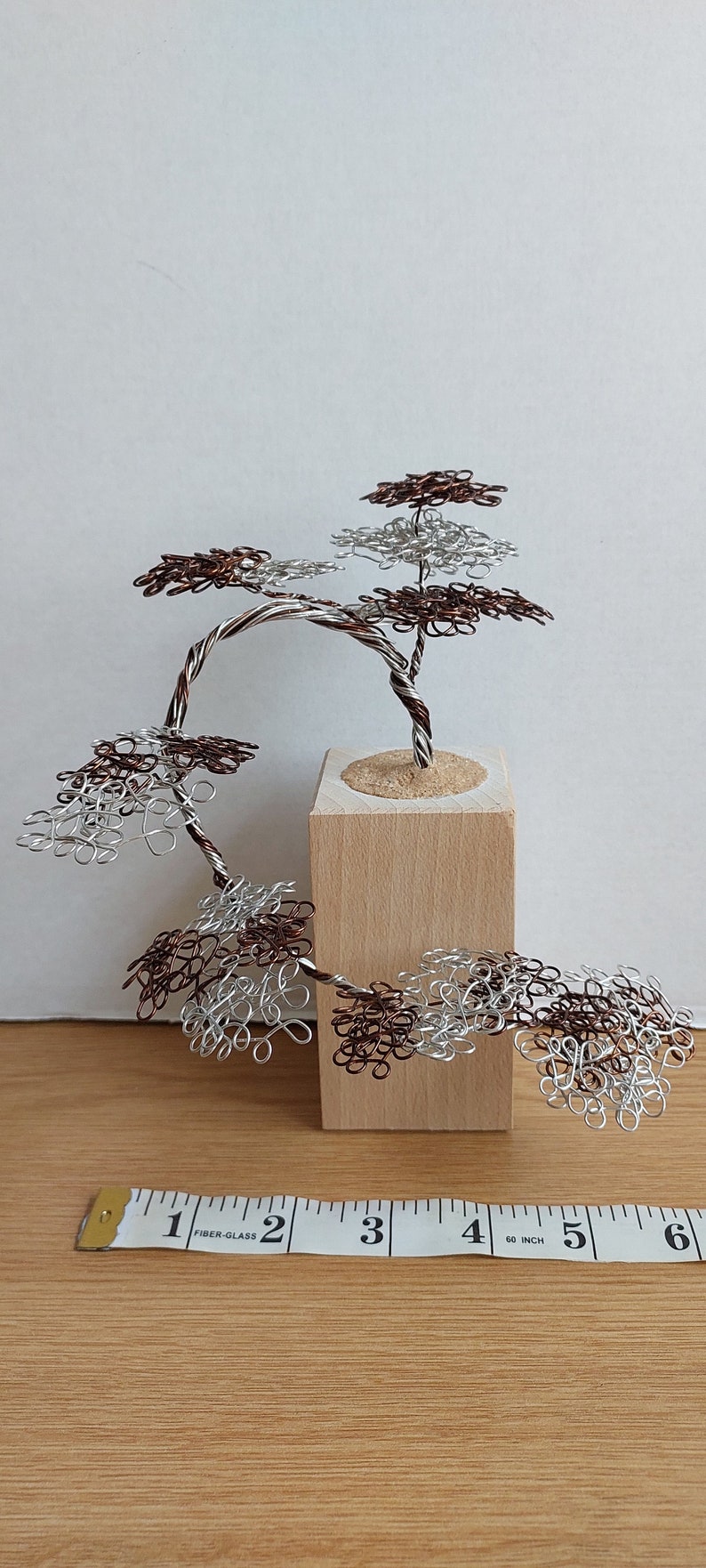 May include: A wire sculpture of a bonsai tree with brown and silver wire branches and leaves. The tree is mounted on a small wooden base.