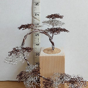 May include: A wire sculpture of a tree with brown and silver wire branches. The tree is about 5 inches tall and is sitting on a wooden base.