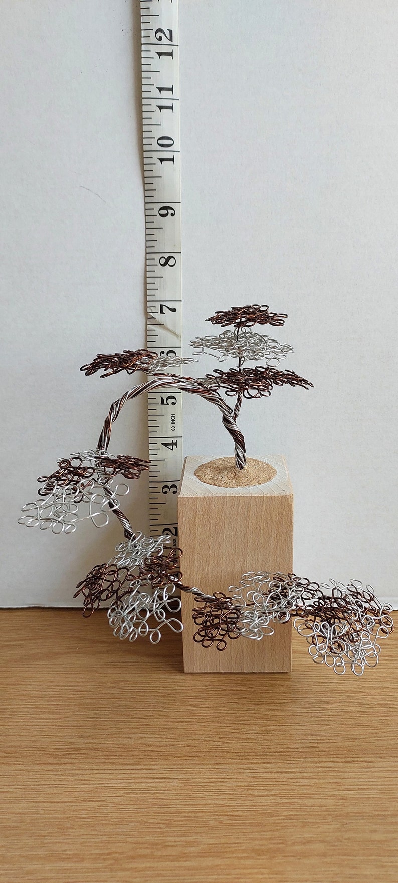 May include: A wire sculpture of a tree with brown and silver wire branches. The tree is about 5 inches tall and is sitting on a wooden base.