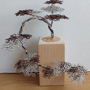 May include: A wire sculpture of a tree with multiple branches and leaves made of silver and copper wire. The tree is mounted on a wooden base.