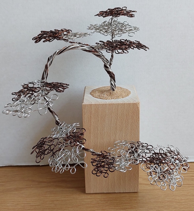 May include: A wire sculpture of a tree with multiple branches and leaves made of silver and copper wire. The tree is mounted on a wooden base.