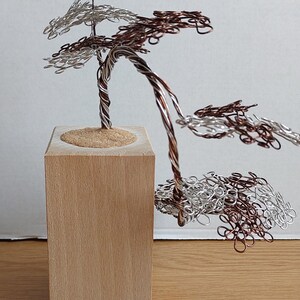 May include: A wire sculpture of a tree with brown and silver wire branches. The tree is sitting on a wooden base.