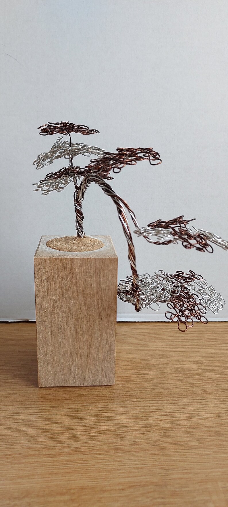May include: A wire sculpture of a tree with brown and silver wire branches. The tree is sitting on a wooden base.