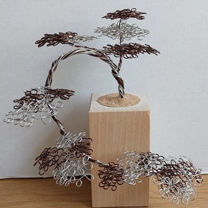 May include: A wire sculpture of a bonsai tree with brown and silver wire branches and leaves. The tree is mounted on a wooden base.