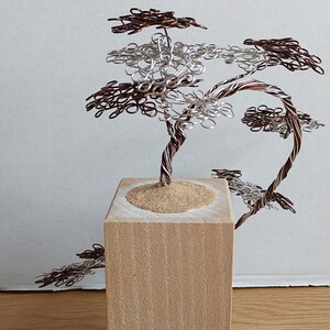 May include: A wire sculpture of a tree with brown and silver wire branches. The tree is sitting on a wooden base.