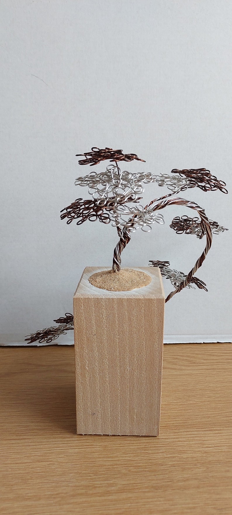May include: A wire sculpture of a tree with brown and silver wire branches. The tree is sitting on a wooden base.