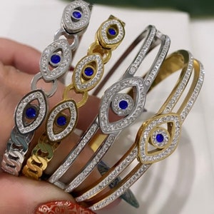 May include: Four gold and silver bracelets with blue evil eye charms and clear crystal accents. The bracelets are stacked on top of each other.