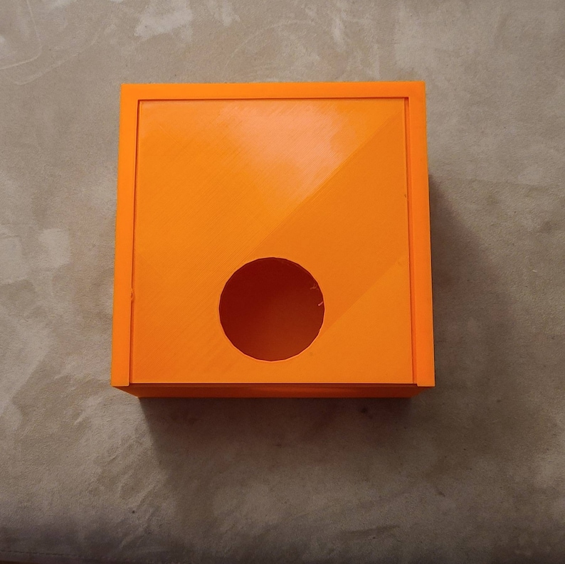 May include: Orange plastic box with a round hole in the front. The box is designed to hold tissues.