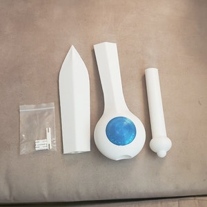 Op de afbeelding: Een wit 3D-geprint zwaard met een blauwe cirkel op het handvat. Het zwaard bestaat uit drie delen: het blad, het handvat en de pommel. De pommel is een apart deel dat aan het handvat kan worden bevestigd.