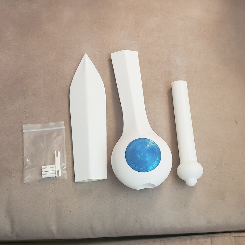 Op de afbeelding: Een wit 3D-geprint zwaard met een blauwe cirkel op het handvat. Het zwaard bestaat uit drie delen: het blad, het handvat en de pommel. De pommel is een apart deel dat aan het handvat kan worden bevestigd.
