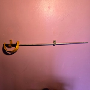 May include: A yellow metal sword holder mounted on a pink wall with a silver metal sword hanging from it.