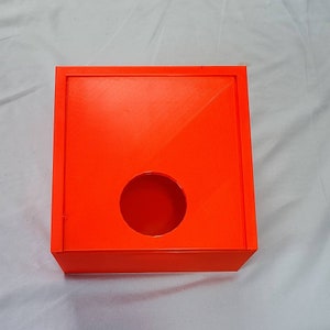 May include: A bright orange square box with a round hole in the centre. The box has a lid that is slightly ajar.