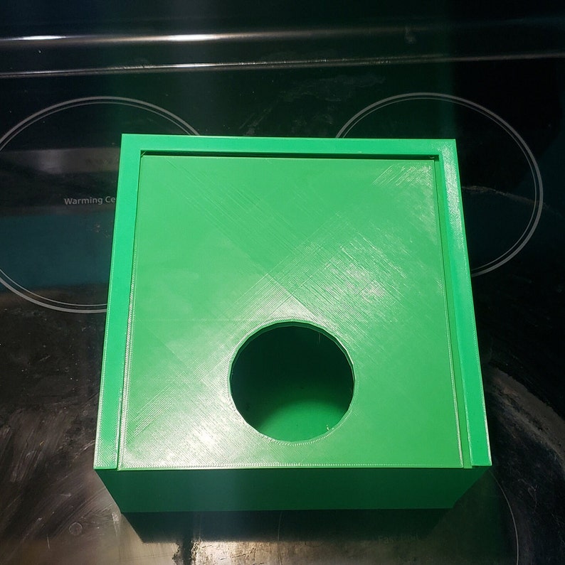 May include: A bright green plastic tissue box with a round opening in the front. The box has a smooth, slightly textured surface.