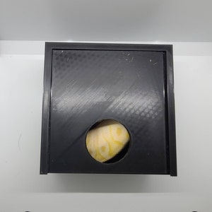 May include: A black plastic box with a round hole in the front. A yellow and white patterned fabric is visible through the hole.