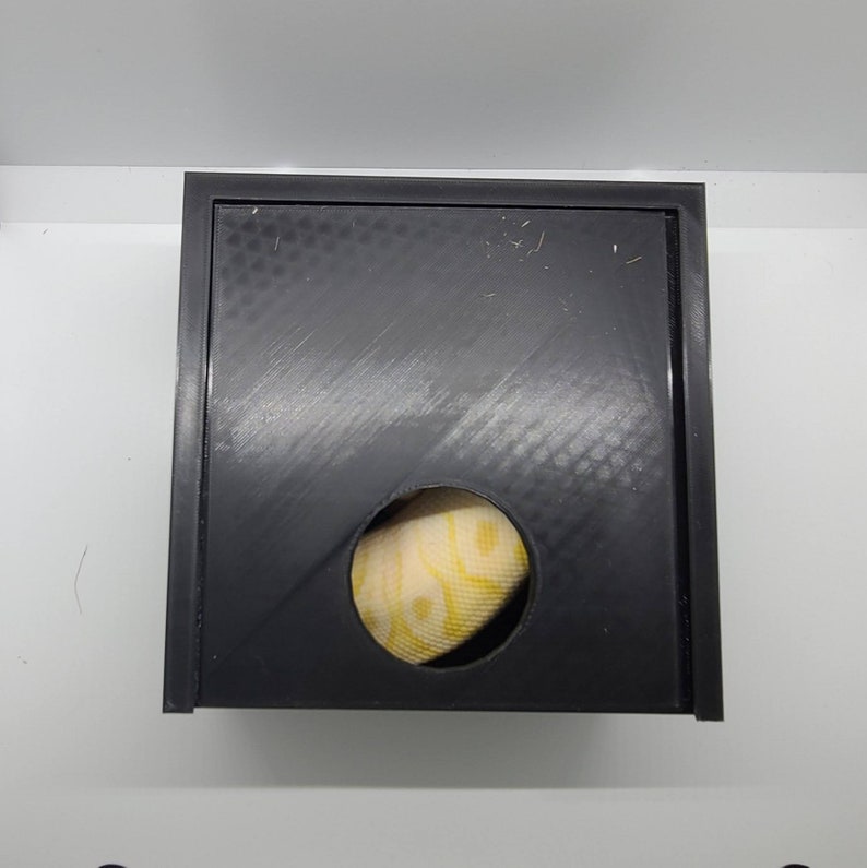 May include: A black plastic box with a round hole in the front. A yellow and white patterned fabric is visible through the hole.