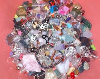 Pode incluir: Uma coleção de pedras preciosas polidas, berloques de metal e gaiolas de arame para contas em um recipiente rosa. A mistura inclui símbolos yin-yang, berloques de sol, chaves pequenas e vários cristais coloridos como quartzo rosa e ametista.