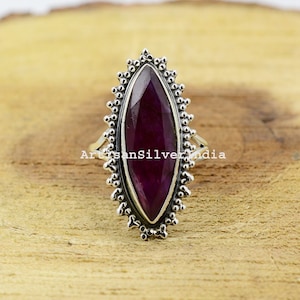 以下が含まれることがあります： 装飾的な波状のベゼルにセットされた、濃い紫色のマルキーズ型の宝石が施されたスターリングシルバーのリングです。