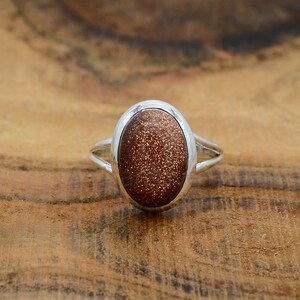 May include: A silver ring with a brown oval-shaped sunstone gemstone.