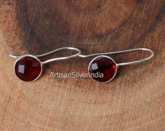 May include: A pair of silver earrings with red gemstone accents. The earrings have a simple hook design.