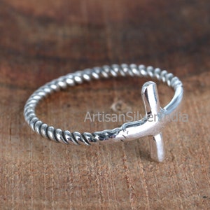 May include: A silver ring with a twisted band and a simple cross design.