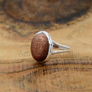 May include: A silver ring with a brown oval sunstone gemstone. The ring has a simple band with a slightly raised edge around the stone.