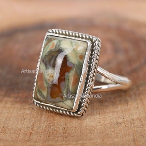 May include: A silver ring featuring a rectangular green, brown and white stone set in a braided silver bezel.