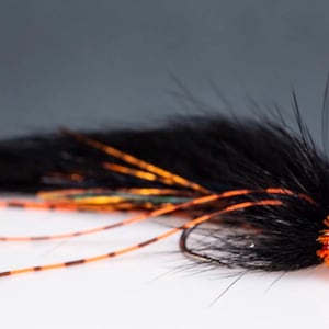May include: A black and orange fly fishing lure with a long, bushy tail and a bright orange head.