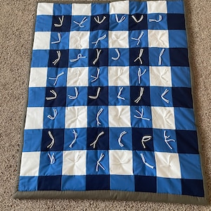 May include: A blue and white checked baby quilt with white knotted ties. The quilt has a grey border.