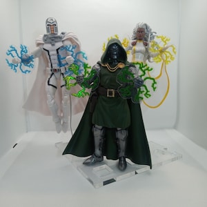 May include: Three action figures of Marvel Comics characters: Magneto in a white and blue costume, Doctor Doom in a green cape and armor, and Storm in a white and yellow costume. Each figure is holding a translucent lightning bolt effect piece.