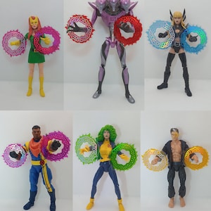 Puede incluir: Seis figuras de acción, cada una sosteniendo un par de armas circulares con forma de sierra. Las figuras están en varias poses y atuendos, con una gama de colores que incluyen verde, morado, azul y amarillo. Las armas tienen una apariencia translúcida e iridiscente.
