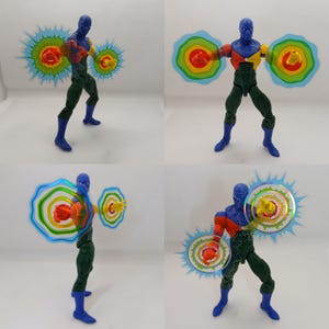以下が含まれることがあります： 青、赤、黄色のフィギュアで、緑色のズボンと青いブーツを履いています。2つの半透明でカラフルなエネルギーブラストを持っています。白い背景に対して、さまざまなポーズで表示されています。