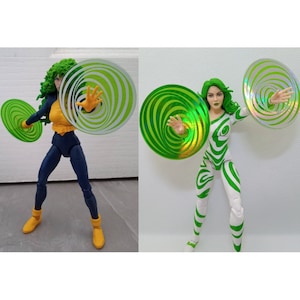 May include: Two action figures of a female superhero with green hair and a white and green costume. The figures are holding green and white swirling discs in their hands.