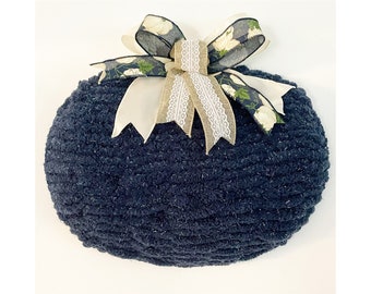 May include: A navy blue, round, fluffy wreath with a white and green floral ribbon tied in a bow.