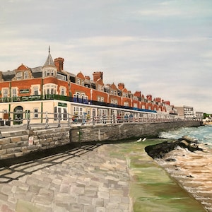 May include: A painting of a row of brick buildings along a waterfront with a stone walkway and a sandy beach in the background.