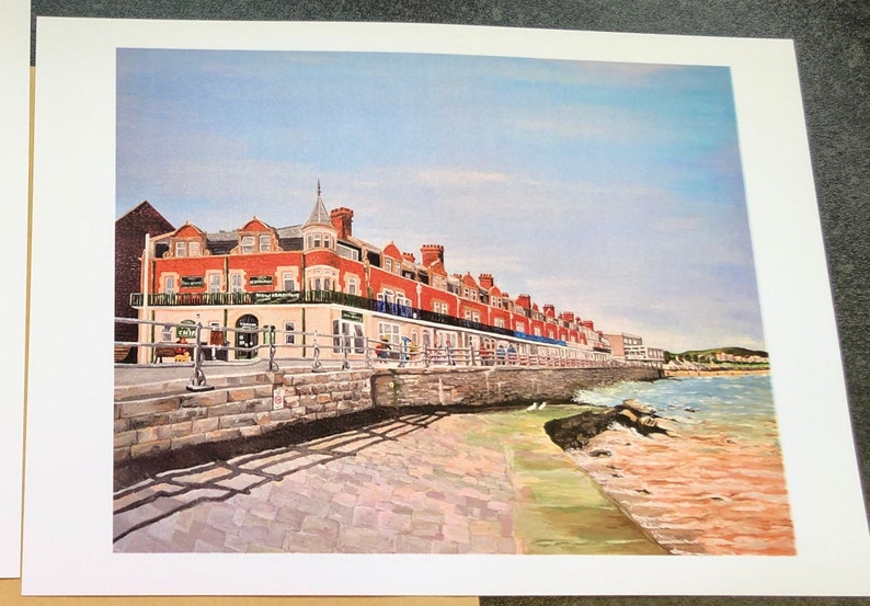 May include: A painting of a red brick building with a white trim, located on a waterfront. The building has a row of windows and a balcony. The building is surrounded by a stone wall and a cobblestone walkway. The water is blue and there are white birds in the water.
