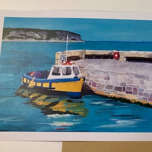 May include: A yellow and blue fishing boat is docked at a stone pier. The boat has a white cabin and a life ring hanging on the side. The water is blue and there is a green hill in the background.