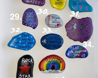 May include: A collection of 10 painted rocks with inspirational messages. The rocks are painted in various colors, including purple, blue, yellow, and green. The messages include "It's a good day to be happy", "Believe in yourself", "Don't let anyone ever dull your sparkle", and "Let life surprise you".