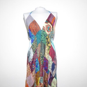 Pode incluir: Um vestido halter de patchwork com decote em V. O vestido apresenta uma variedade de retalhos de tecido coloridos em tons de vermelho, azul, verde e laranja. O vestido é exibido em um manequim branco sobre um fundo branco.