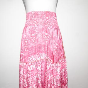 Può includere: Una gonna rosa e bianca a strati con un motivo floreale. La gonna ha una fascia elastica e una silhouette fluida.