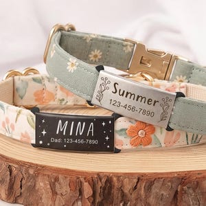 May include: Two pet collars with metal buckles and personalized nameplates. One collar is sage green with white daisies, featuring a silver plate engraved with "Summer" and "123-456-7890". The other is cream with orange flowers, featuring a black plate with "MINA" and "Dad: 123-456-7890".