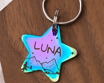 May include: A rainbow iridescent star-shaped pet tag with a mountain scene and the name "LUNA" engraved on it. The tag is attached to a silver key ring.