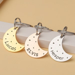 May include: Three silver crescent moon keychains with star accents. The keychains are engraved with the names Lucas, Elvis, and Hesper.