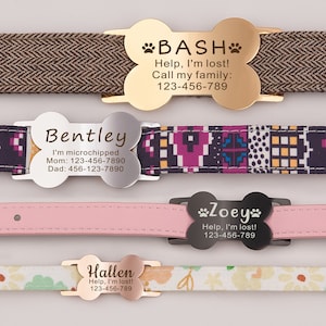 May include: Four dog ID tags with bone-shaped designs. The tags are made of gold, silver, and black metal. The tags have engraved text with the dog's name, a message, and phone numbers. The tags are attached to different colored dog collars.